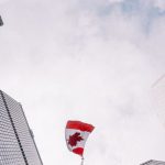 Corporate Governance - From below of perspective tunnel between glass skyscrapers and pole with fluttering flag of Canada