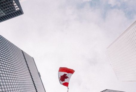 Corporate Governance - From below of perspective tunnel between glass skyscrapers and pole with fluttering flag of Canada