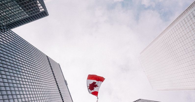 Corporate Governance - From below of perspective tunnel between glass skyscrapers and pole with fluttering flag of Canada
