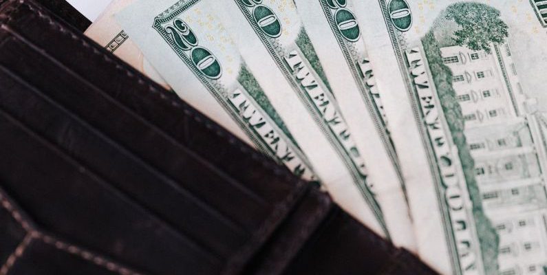 Market Opportunities - From above of black leather wallet with cash money of twenty dollars placed on white table