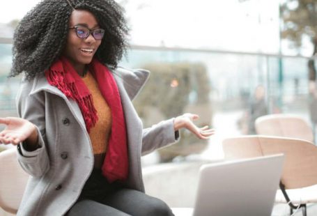 Video Content - Happy excited African American female laughing and gesticulating while having video calling on laptop and sitting at modern cafe